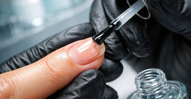 A professional nail technician applying a clear, strengthening treatment to a client's natural nails in a modern salon setting.