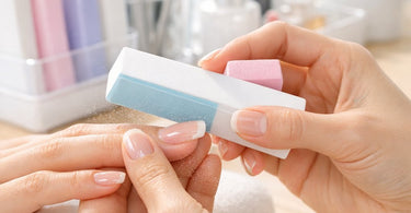Close-up of a professional nail technician's hands using a white filing block on a clear acrylic nail, with no dust visible.