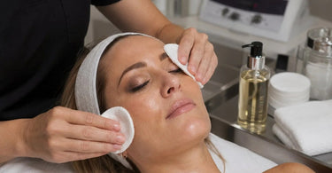 Pre-cleanse oil dissolving long-wear professional makeup on a cotton pad with spa background