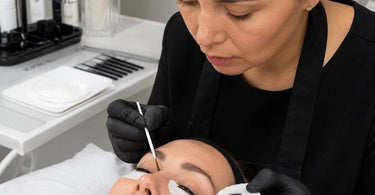Professional lash tinting on lower lashes using a protective shield and precision applicator to avoid skin contact.