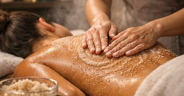 A collection of professional body scrub products and spa tools arranged on a bamboo surface, including jars of sugar scrub, a body brush, and luxurious towels, illustrating key elements for body scrub treatments.