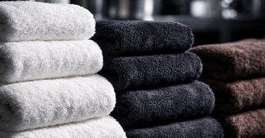 Stack of fluffy white spa towels neatly folded on a shelf, with a single towel unfolded to show its plush texture, representing high-quality linens for a salon or spa.