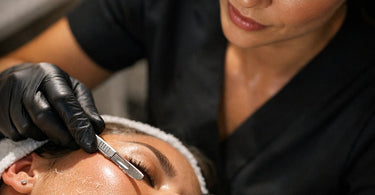 Close-up of a professional esthetician performing a dermaplaning treatment on a client's cheek, showing the precise technique and glowing skin results.