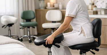 A modern, ergonomic saddle stool with back support in a sleek spa treatment room setting