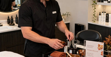 A spa professional demonstrating a seasonal spa service enhancement with aromatherapy oils, towels, and treatment products.