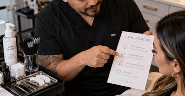 Lash artist demonstrating gentle aftercare cleansing routine to client in a professional spa treatment room