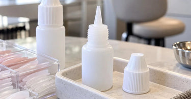 Professional nail glue bottle and precision applicator nozzle at an organized nail salon workstation, illustrating how nail technicians can prevent adhesive nozzles from clogging between clients