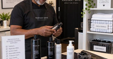 Professional spa towels neatly folded beside sunless tanning supplies and a spray tan applicator, illustrating how to keep sunless tanning supplies from staining towels