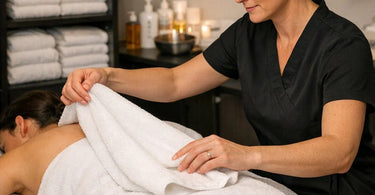 Stack of fluffy white professional grade towels for spa and salon use with a natural green leaf on top.