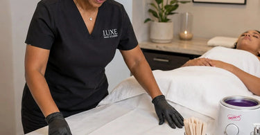 A professional waxing treatment table set up with clean white linens and a brown waxing pad used to prevent wax from sticking to the sheets.