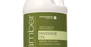 A large one-gallon jug of Amber Products Green Tea Mint Massage Oil, perfect for professional spa and salon use, sitting on a massage table with soft focus background.