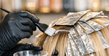 Close-up of a hairstylist applying a protective pre-treatment serum to hair sections before a double-process color service in a salon.