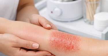 A professional esthetician carefully applying purple rosin-free hard wax to a client's underarm, demonstrating a gentle and precise waxing technique for sensitive skin.