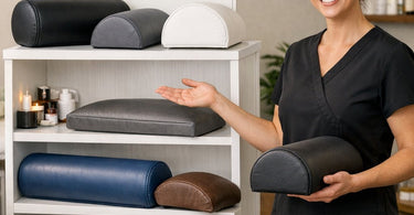 A selection of professional massage bolsters including round, half-moon, and wedge shapes neatly displayed on a white massage table with soft linens.