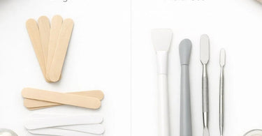 Close-up comparison of single-use wooden spatulas and multi-use metal spatulas on a clean spa towel with wax pots