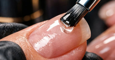 Close-up of a nail technician applying acid-free primer to a client's natural nail, demonstrating precise brushwork for a flawless base.