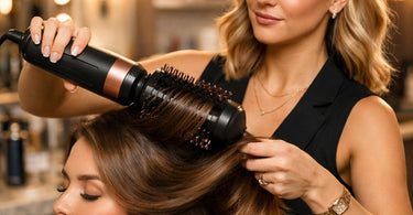 A professional hairstylist demonstrating the use of a blow-dry brush on a client's hair in a modern salon setting.