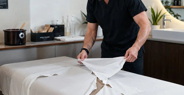 An overhead image illustrating the hidden cost and hygiene issues of using cheap table paper in professional spa, massage, and waxing treatment rooms.