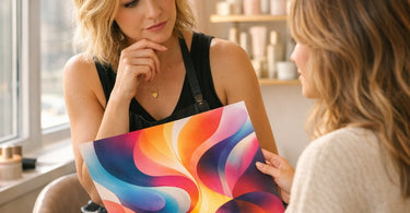 A stylist holding a color swatch book next to a client's phone displaying abstract colorful art, symbolizing the consultation process for interpreting creative hair color goals