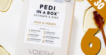Voesh Ultimate Pedicure in a Box 6-Step Kit in Milk & Honey, showing the sealed single-use packets arranged around the box on a spa towel.