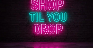 A vibrant pink and blue Shop Til You Drop neon sign glowing in a modern spa or salon setting