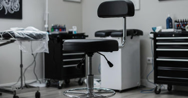 Professional tattoo artist working while sitting on an ergonomic hydraulic stool in a modern studio