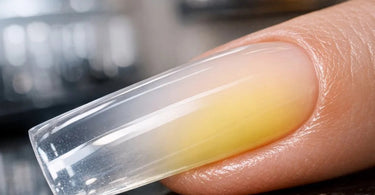 A close-up image of a professional nail technician applying a clear acrylic overlay, highlighting the importance of technique and quality supplies to prevent yellowing.