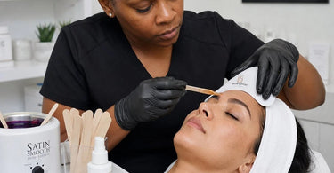 Close up of a professional brow waxing treatment with skin stretching support tools used by an esthetician for precise shaping.