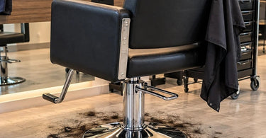 Professional salon styling chair with a hydraulic pedestal base and loose haircut clippings collecting around the bottom on the salon floor