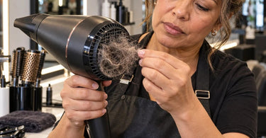 Professional salon hair dryer showing lint and loose hair buildup around the air intake filter, highlighting the importance of regular blow dryer maintenance