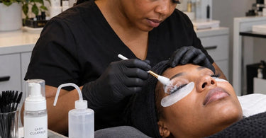 Professional lash artist cleansing a client's eyelash extensions during a fill appointment