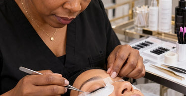 Professional lash artist securing lower lashes beneath under-eye pads and tape during an eyelash extension service