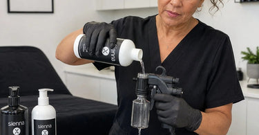 A close-up image showing a professional spray tan gun being flushed and cleaned with warm water to prevent dried solution buildup and maintain equipment performance.
