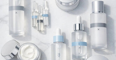 A curated selection of professional skincare bottles and vials containing exfoliants and peptide serums, arranged neatly on a spa towel with a green plant.