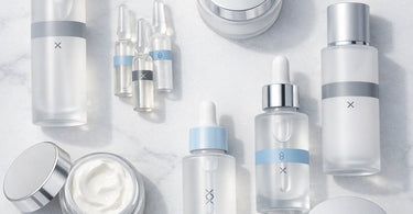 A curated selection of professional skincare bottles and vials containing exfoliants and peptide serums, arranged neatly on a spa towel with a green plant.