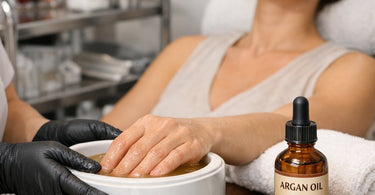 Warm golden argan oil being poured over hands during a professional hot oil manicure treatment at a spa with towels.