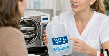 Close up of professional autoclave sterilization machine with a plastic gallon jug of distilled water beside it on a stainless steel counter in a clean spa environment.