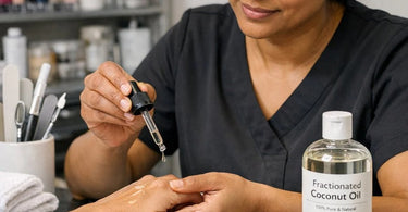 A clear glass bottle of fractionated coconut oil pouring onto a clean white towel with a green botanical leaf, symbolizing non-staining spa treatments.