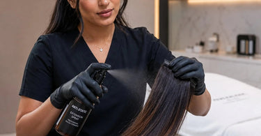 A professional stylist gently brushing long, silky synthetic hair extensions with a wooden brush in a bright, modern salon to neutralize static.
