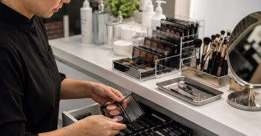 A professional makeup artist's hand holding a highly pigmented eyeshadow palette near an acrylic organizer, illustrating best practices for storing eye palettes.