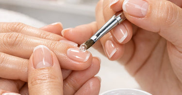 A professional nail technician applying clear builder gel to a client's natural nails with a brush, demonstrating the builder gel for natural nails technique.