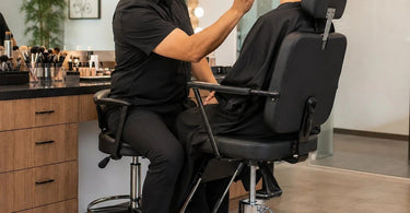 A professional makeup artist working on a client in a high-quality adjustable makeup chair, demonstrating excellent posture and ergonomic setup