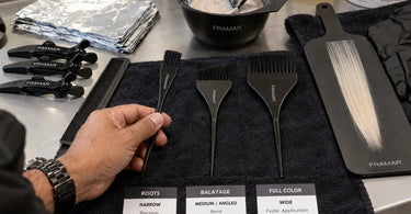 A collection of professional tint brushes of varying widths displayed on a color swatch, symbolizing the choice for roots, balayage, and full color services.