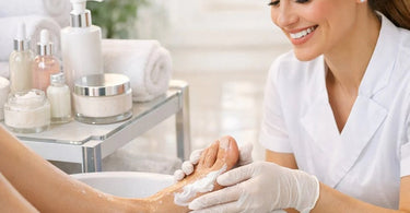 A spa professional performing a luxury pedicure, applying cream to a client's foot, with professional callus softening products and tools visible.