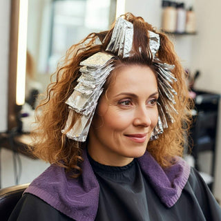 A client with curly hair in foils, getting her hair colored at a salon.