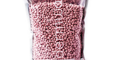 A bag of Dermwax Pink Chiffon Hard Wax Beads on a spa table with flowers