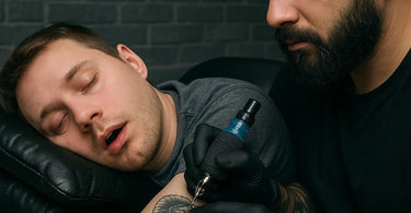 Tattoo artist working on sleeping client in professional studio environment