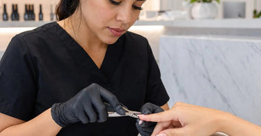 Professional nail technician using pinching clamps to shape the perfect C-curve on a client's nail enhancement at a salon.