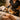Close-up of a professional esthetician's hands preparing warm hard wax with a spatula for a Brazilian wax service, with clean towels and waxing supplies in the background.