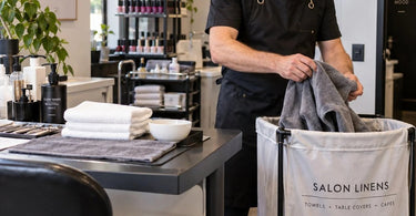 Professional salon and spa linens organized for end-of-day laundry handoff with towel steamer and rolling hampers